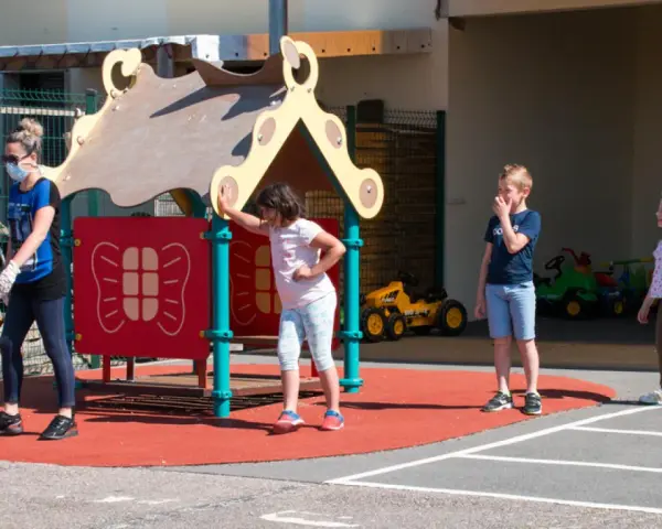 Une animatrice, masque et gants, surveille des enfants sur un terrain de jeu. Le directeur ACM veille à la sécurité.