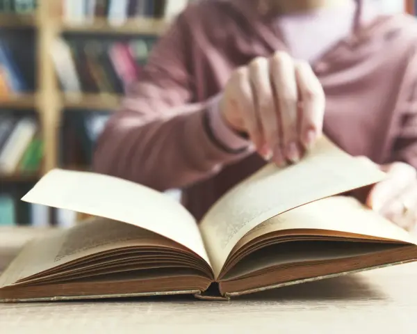 Otwarta księga na stole, w tle regały pełne książek. To początek podróży przez arcydzieła literatury światowej, lista skarbów do odkrycia.
