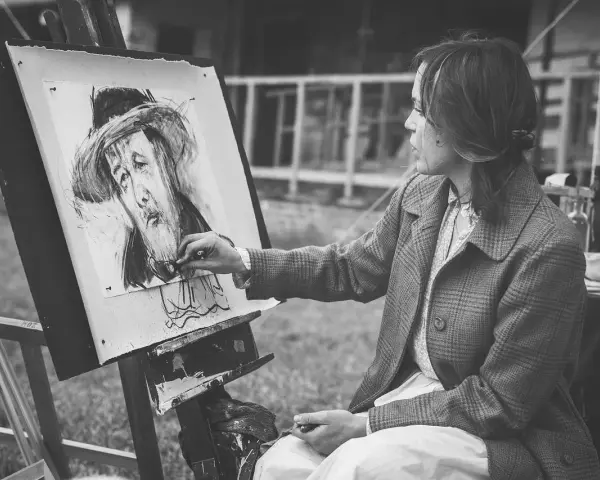 Artystka tworzy portret węglem. Jej ręka z pędzlem zbliża się do płótna, gdzie widoczna jest plama rysunek.