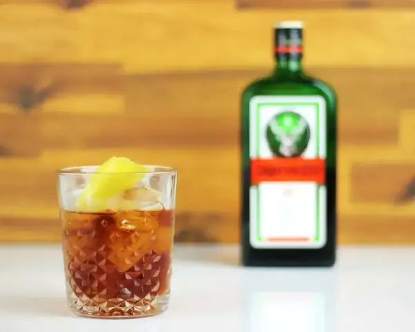 Jägermeister z pomarańczą to świetny drink. Na zdjęciu drink z lodem i plasterkiem pomarańczy obok butelki Jägermeister.
