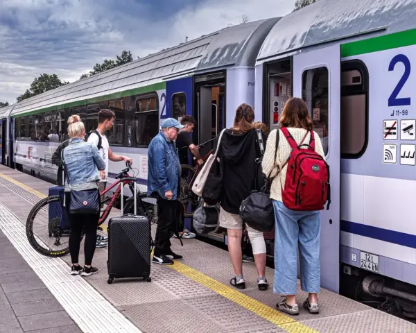 Ludzie z bagażami i rowerami czekają na pociąg. Warto sprawdzić dostępne zniżki i ulgi na podróż.