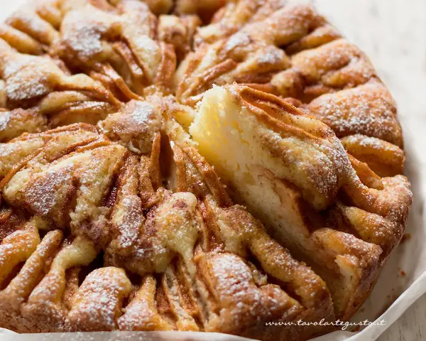 Una deliziosa torta di mele, cosparsa di zucchero a velo, con una fetta appena tolta che rivela la morbidezza dell'impasto e le mele caramellate.