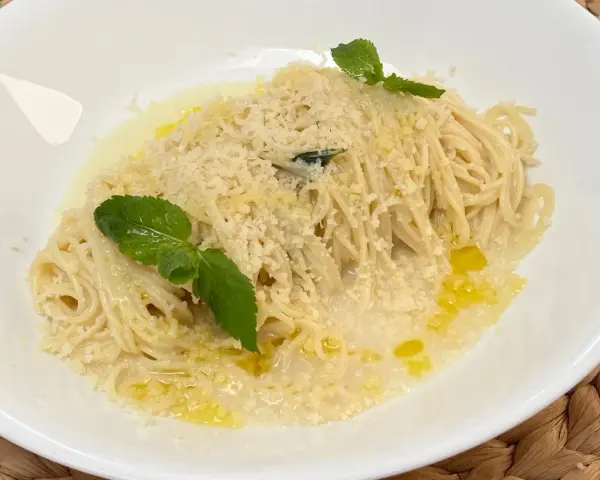 Spaghetti al limone cremosi, cosparsi di parmigiano e guarniti con foglie di menta fresca. Un piatto profumato e invitante.