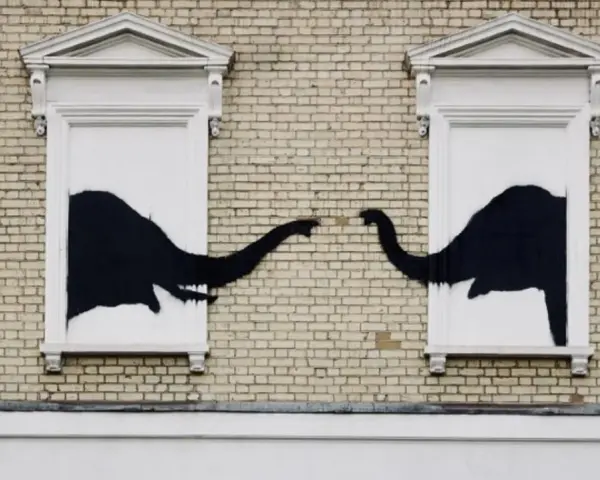 Œuvre Banksy : deux éléphants noirs se touchent la trompe à travers deux fenêtres sur un mur de briques.