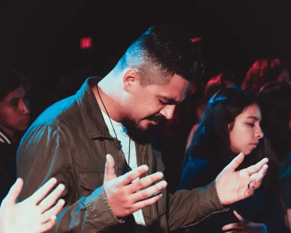 A man with his hands raised in prayer, part of a congregation following the order of prayer.