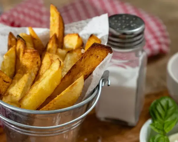 Złociste frytki w metalowym wiaderku, obok solniczka i ketchup. Czy ziemniaki sałatkowe nadają się na frytki? Wyglądają pysznie!