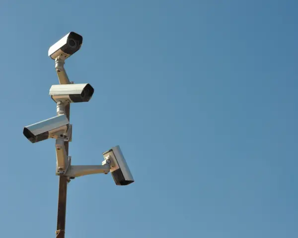 Cztery kamery monitoringu na słupie, czujne oko inwigilacji wpatrujące się w błękitne niebo.