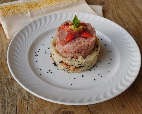 Due torri di riso, una rosa con fragole e menta, l'altra bianca con verdure e semi neri. Un piatto che ricorda la crema di riso.