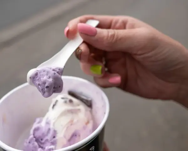 Eine Hand mit pink lackierten Nägeln hält einen Löffel mit zwei Kugeln Eis im Becher, italienisch.