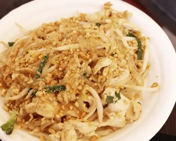 Pyszny pad thai oryginalny przepis z kurczakiem, kiełkami i orzeszkami ziemnymi na białym talerzu.