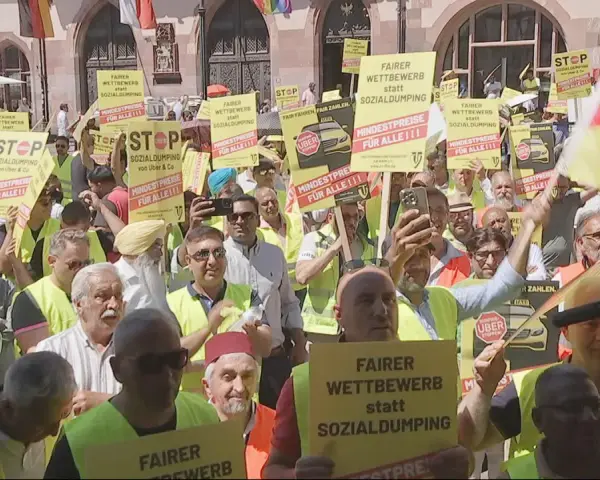 Demonstranten mit gelben Schildern fordern "Fairer Wettbewerb statt Sozialdumping" und "Mindestpreise für alle". Ein **Taxi-Streik** ist im Gange.