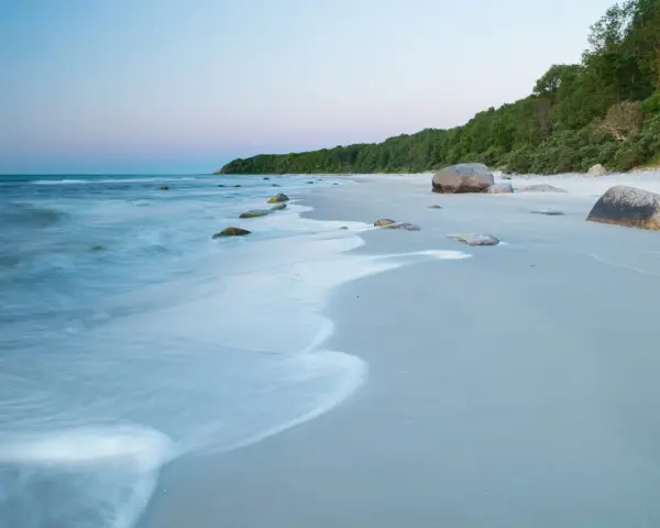 Spokojne plaże nad Bałtykiem o świcie, z delikatnymi falami i kamieniami na piasku.