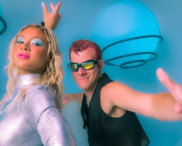 Un groupe hollandais des années 90, avec une femme au maquillage bleu vif et un homme aux lunettes futuristes, pose devant des sphères lumineuses bleues.