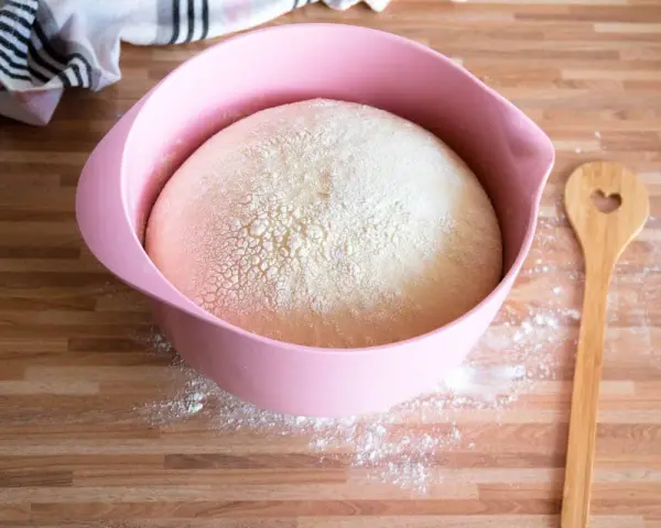 Ein aufgegangener Teig in einer rosa Schüssel, bereit zum Backen. Daneben liegt ein Holzlöffel mit Herz. Was ist Germ?