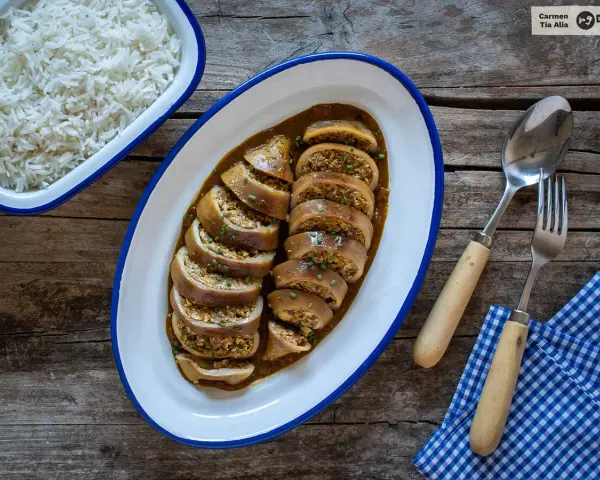 Calamares rellenos en salsa, servidos en una bandeja ovalada junto a un bol de arroz blanco. Cubiertos con cebollino picado.