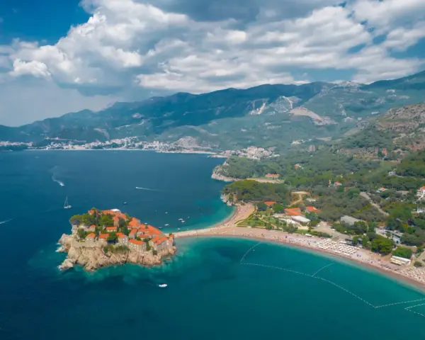 Sveti Stefan, Czarnogóra czy warto? Widok z lotu ptaka na malowniczą wyspę połączoną z lądem, turkusowe morze i górzyste wybrzeże.