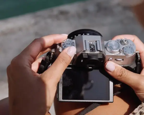 Dłonie trzymają srebrny aparat Fujifilm XT50, obracając pokrętło trybów filmowych.