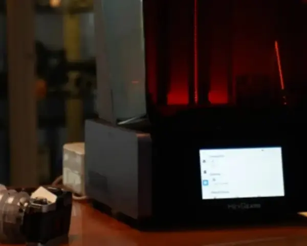 A HeyGears resin printer with a red interior light. Beside it, a camera lens. This setup hints at the process of how long to cure resin prints.