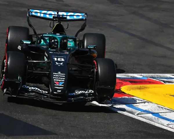 El coche de F1 Aston Martin número 18 se inclina en una curva, con sus neumáticos rozando la línea de la pista.