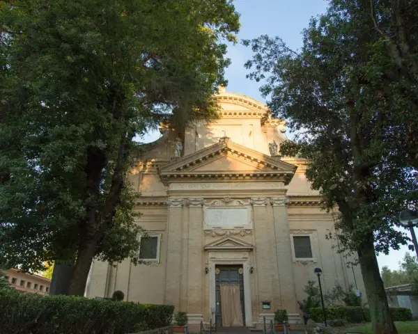 A serene church facade at Tre Fontane, Rome, bathed in golden light, framed by lush green trees.