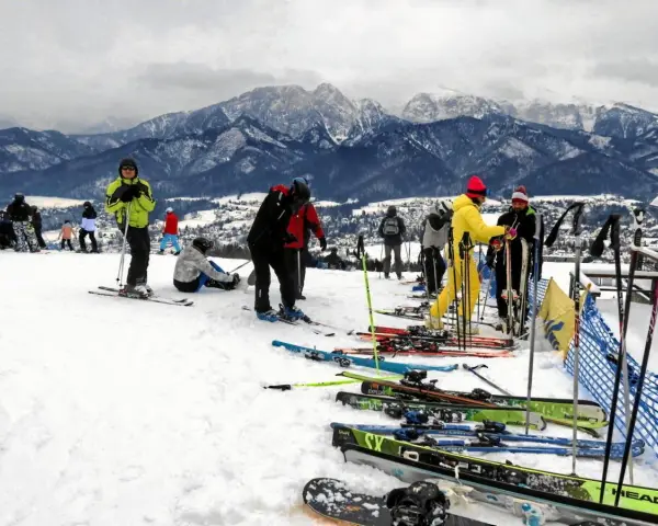 Ludzie na nartach i snowboardach na stoku, w tle góry. Zastanawiasz się, ile się idzie na Gubałówkę? Tu jest zimowo i aktywnie!