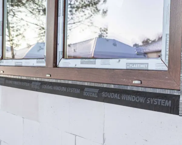 Ciepły montaż okien z użyciem taśmy Soudal Window System. Brązowa rama okienna na tle białego pustaka.