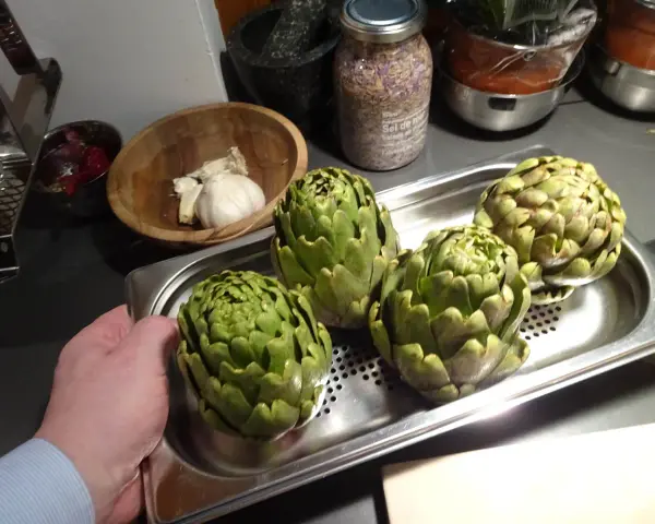 Quatre artichauts verts prêts pour la cuisson vapeur. Une main tient le plateau.