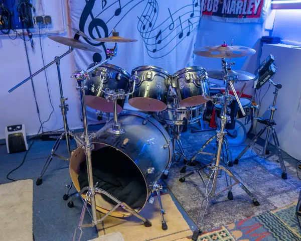 Der **Aufbau Schlagzeug** ist bereit für den nächsten Gig. Glänzende Trommeln und Becken stehen auf stabilen Stativen, beleuchtet von blauem Licht.