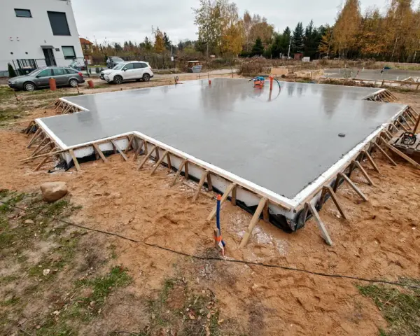 Świeżo wylany beton na budowie. To solidne, najtańsze fundamenty pod przyszły dom, otoczone drewnianym szalunkiem.