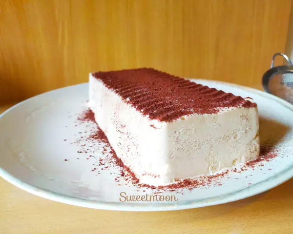 Un delizioso semifreddo al caffè, cosparso di cacao amaro, attende su un piatto bianco.