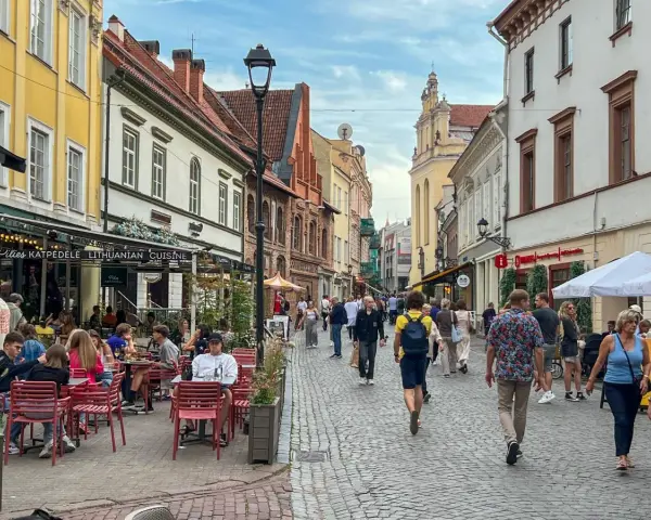 Tłum ludzi spaceruje brukowaną ulicą w Wilnie, siedząc przy stolikach restauracyjnych. Czy wyjazd na Litwę jest bezpieczny? Wygląda na to, że tak!