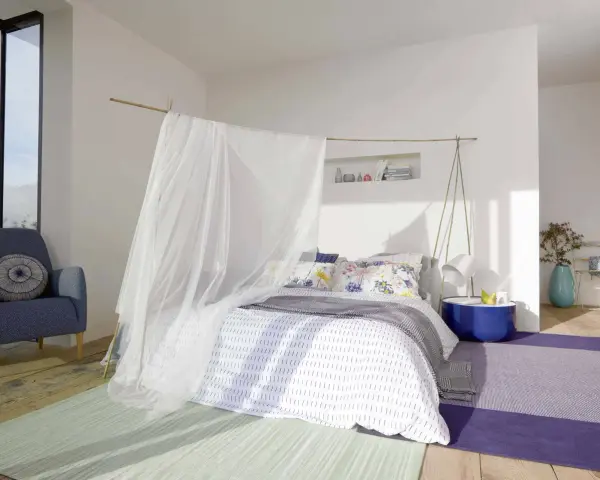 Acogedora habitación marinera con cama con dosel de tul, sillón azul y alfombras de colores.