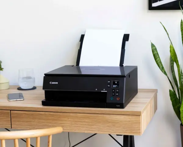 Schwarzer Canon Pixma Drucker mit WLAN verbinden. Ein Smartphone und ein Glas Wasser stehen daneben.