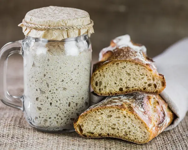 Ein Glas Sauerteig und zwei frisch gebackene Brotscheiben. So ist Sauerteig als Brot ein Genuss.