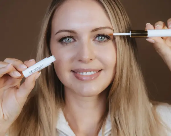 Frau mit blauen Augen trägt ein Serum auf ihre Wimpern auf, um sie wachsen zu lassen.
