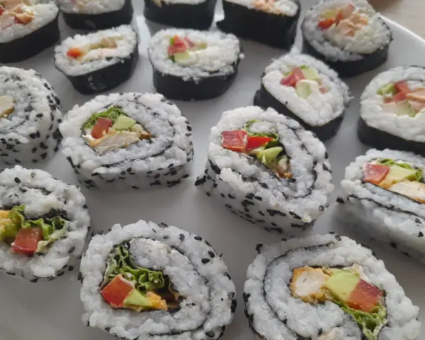 Pyszne domowe sushi z kurczakiem, awokado i warzywami, posypane czarnym sezamem.