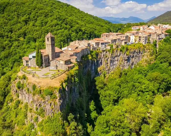 Un borgo medievale, Castellfollit de la Roca, aggrappato a una scogliera basaltica, circondato da lussureggianti foreste verdi.