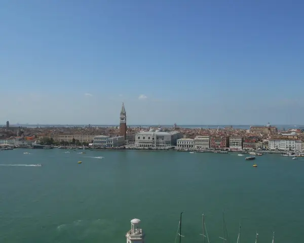 Venezia dall'alto, con il Campanile di San Marco che svetta tra i tetti rossi e il Canal Grande animato da vaporetti e barche.