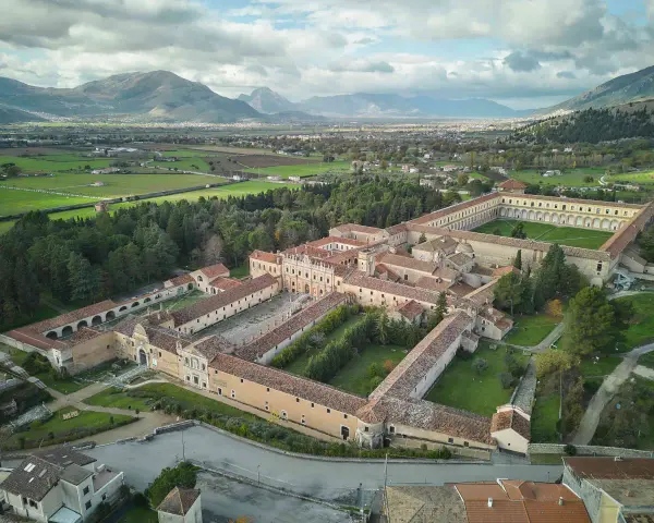 Vasta Certosa di Padula, un complesso monastico imponente con cortili verdi, circondato da alberi e montagne sullo sfondo.