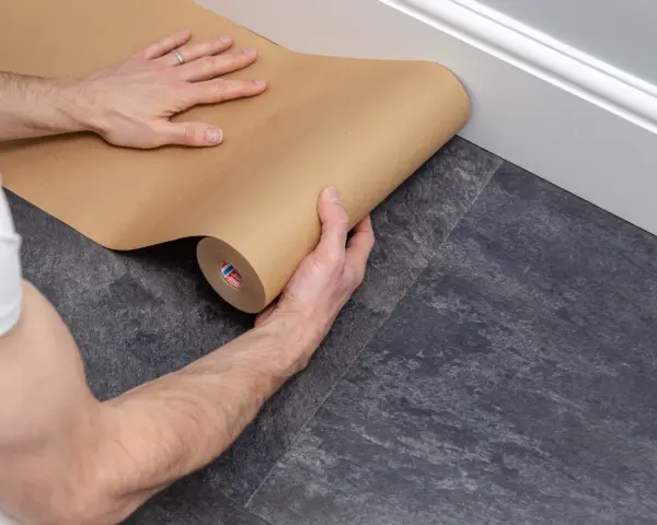 Ręce rozwijają brązowy papier, zabezpieczając podłogę podczas remontu.