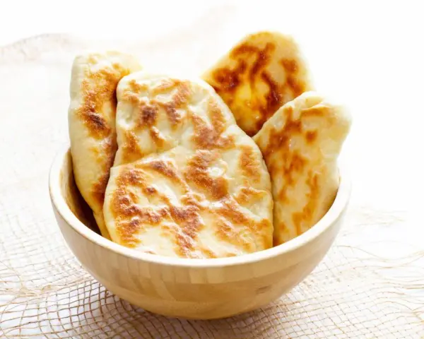 Kilka świeżo upieczonych chlebków naan w drewnianej misce.