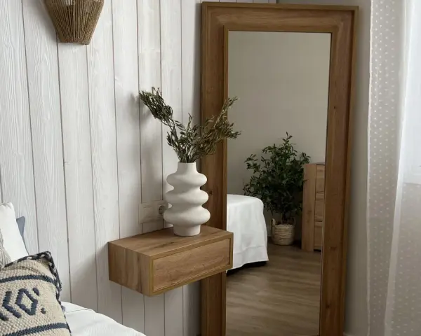 Estantería flotante de madera con jarrón blanco y ramas secas, ideal para ideas para decorar rincones pequeños. Reflejo de planta y cama en espejo grande.
