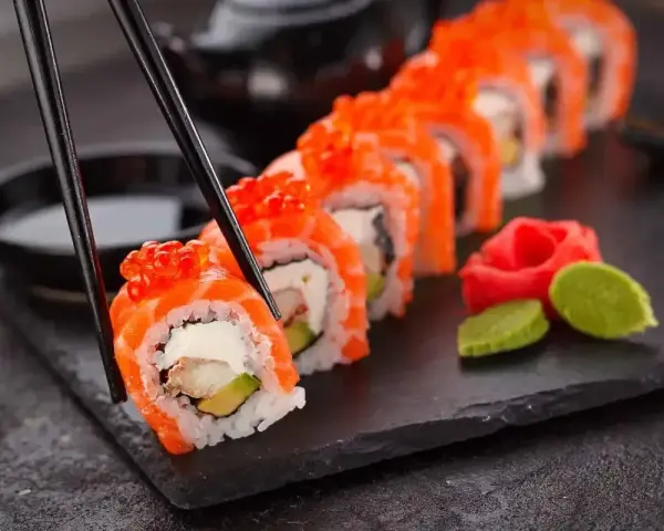 Chopsticks podnoszą kawałek sushi z łososiem i ikrą. Czy sushi jest lekkostrawne? Zależy od składników, ale ten wygląda apetycznie.