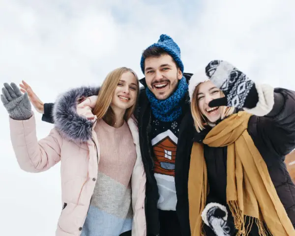 Drei Freunde genießen das Wandern im Winter. Sie tragen warme Kleidung wie Daunenjacken, Mützen und Handschuhe.