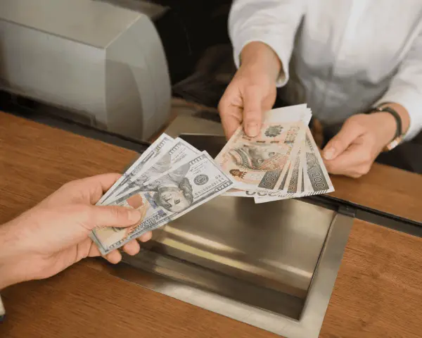 Dwie ręce wymieniają banknoty. Jedna trzyma banknoty 100 dolarów, druga polskie 200 złotych.