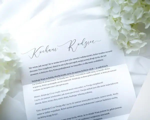 List do rodziców z podziękowaniami. Białe kwiaty i elegancka koperta tworzą tło dla wzruszających słów.