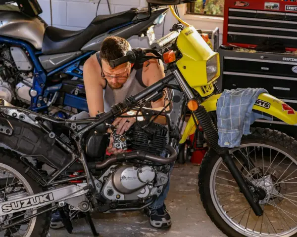 Mężczyzna majstruje przy żółtym motocyklu Suzuki. Rozrusznik kręci, a motocykl nie odpala.