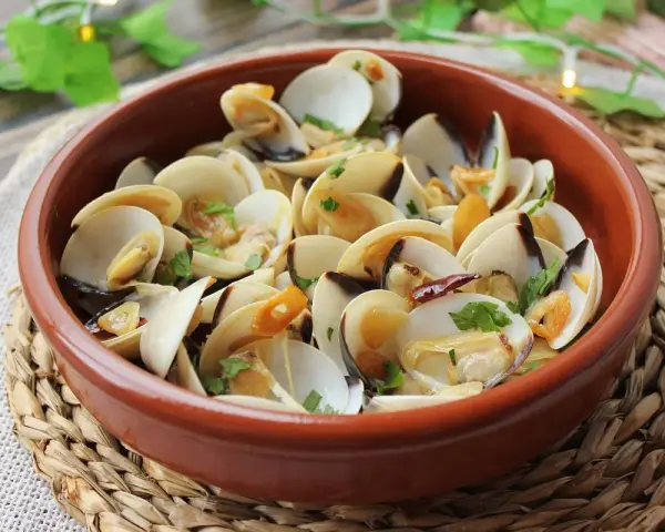 Deliciosas almejas al ajillo, servidas en una cazuela de barro, con ajo laminado y perejil fresco.