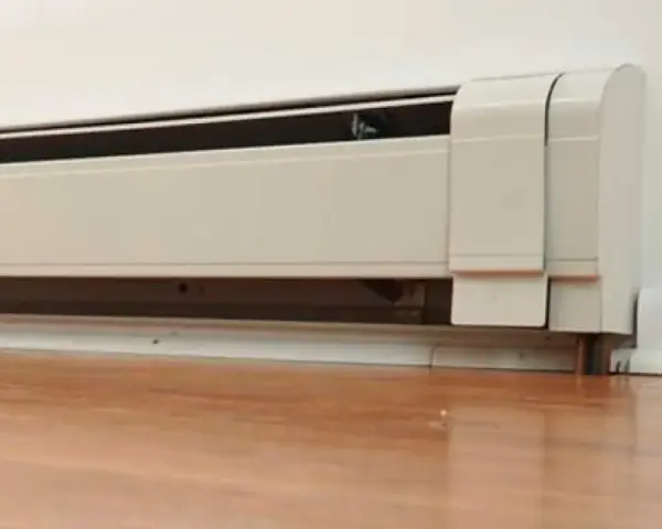 Un zócalo radiante blanco instalado en una pared, con el suelo de madera. Sus desventajas pueden incluir la estética o la distribución del calor.