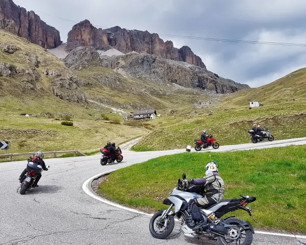 Motociclisti affrontano tornanti sui **Dolomiti passi**, con imponenti vette sullo sfondo.